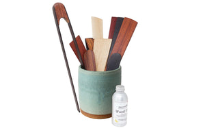 Set of wooden utensils in a teal holder with a bottle of wood care product on a white background